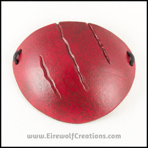 A handmade leather eye patch with three jagged scars carved diagonally, dyed and painted a mottled red reminiscent of blood, for a masquerade costume or assassin or pirate cosplay. By Erin Metcalf of Eirewolf Creations.