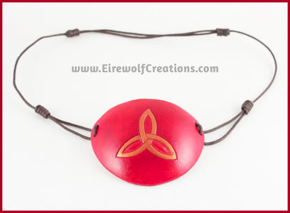 A handmade leather eye patch with a triquetra, or Celtic trinity knot, carved and painted copper on a dyed red background, for a masquerade costume or pirate cosplay. By Erin Metcalf of Eirewolf Creations.