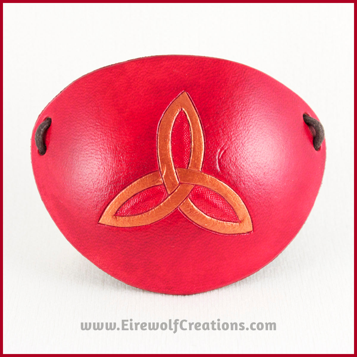 A handmade leather eye patch with a triquetra, or Celtic trinity knot, carved and painted copper on a dyed red background, for a masquerade costume or pirate cosplay. By Erin Metcalf of Eirewolf Creations.