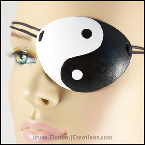 A handmade leather eye patch with a bold black and white yin yang symbol carved and painted over the whole eye patch, for a masquerade costume or pirate cosplay. By Erin Metcalf of Eirewolf Creations.