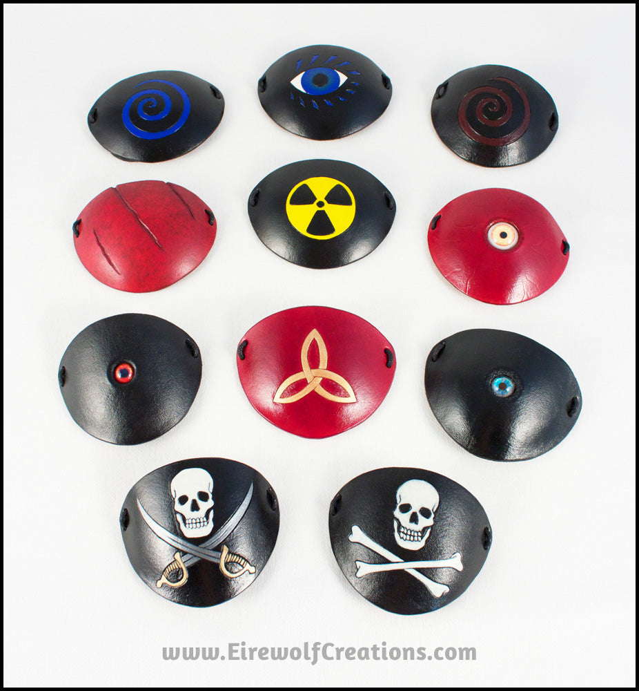 Leather eye patches of varying designs, including spirals, scarred, radiation hazard symbol, eyeballs, Celtic knot, and Jolly Rogers, handmade by Erin Metcalf of Eirewolf Creations.