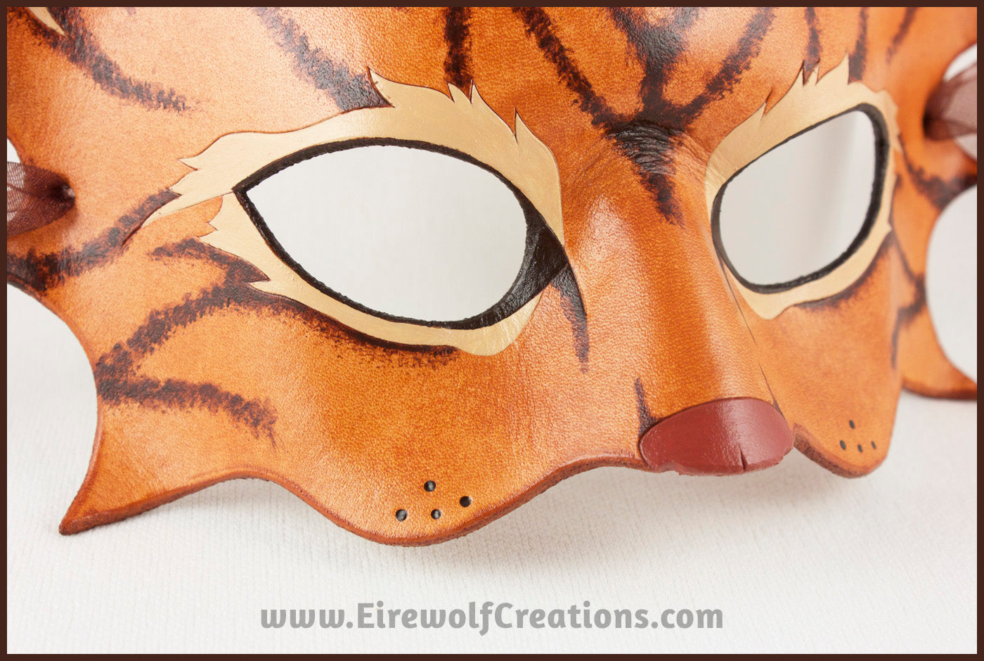 Closeup of a handmade leather tabby cat mask for a masquerade costume, light brown with handpainted dark brown stripes and a dark pink nose and inner ears. By Erin Metcalf of Eirewolf Creations.