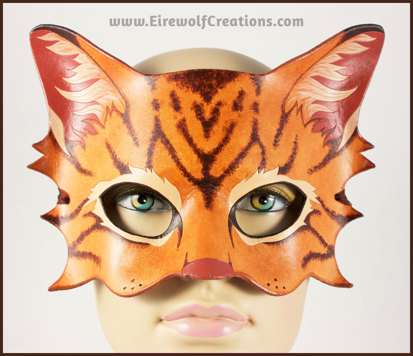 A handmade leather tabby cat mask for a masquerade costume, light brown with handpainted dark brown stripes and a dark pink nose and inner ears. By Erin Metcalf of Eirewolf Creations.