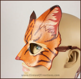 A handmade leather tabby cat mask for a masquerade costume, light brown with handpainted dark brown stripes and a dark pink nose and inner ears. By Erin Metcalf of Eirewolf Creations.