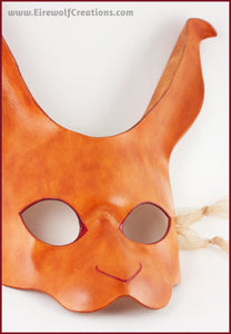 A handmade leather rabbit mask for a masquerade costume, dyed light brown with subtle red details painted around the eyes and nose. By Erin Metcalf of Eirewolf Creations.