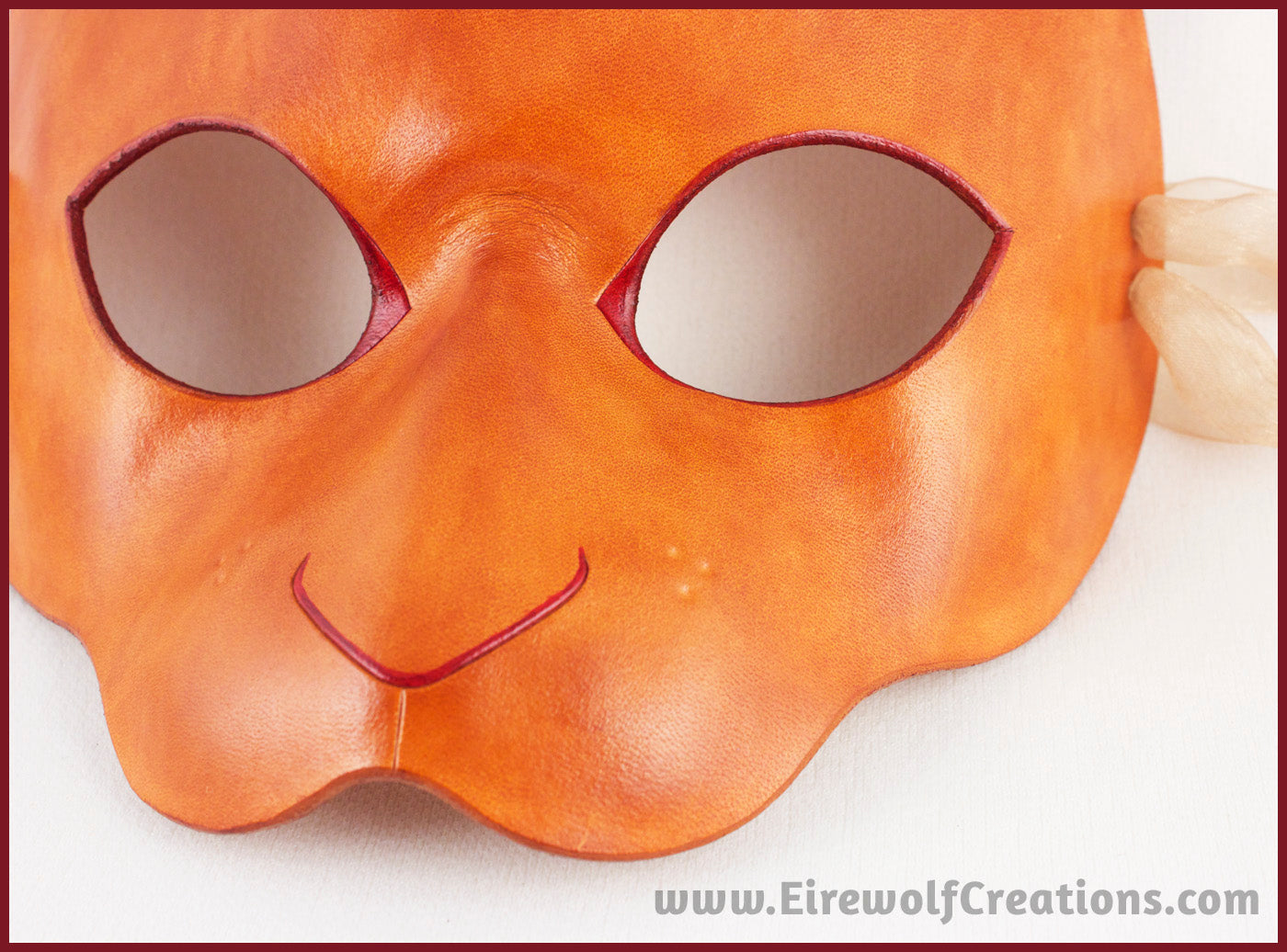 Closeup of a handmade leather rabbit mask for a masquerade costume, dyed light brown with subtle red details painted around the eyes and nose. By Erin Metcalf of Eirewolf Creations.