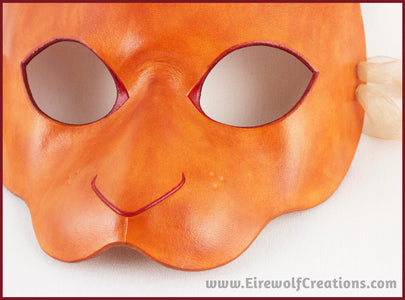 Closeup of a handmade leather rabbit mask for a masquerade costume, dyed light brown with subtle red details painted around the eyes and nose. By Erin Metcalf of Eirewolf Creations.