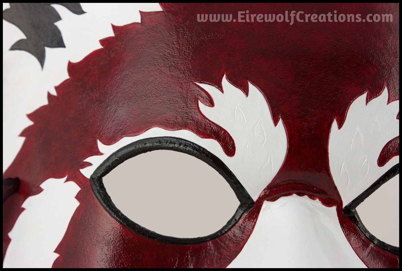 Closeup of a handmade leather Red Panda masquerade mask with bold facial markings carved and painted on the leather. By Erin Metcalf of Eirewolf Creations.